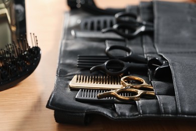 Photo of Hairdresser tools. Professional scissors and combs in leather organizer on wooden table, closeup