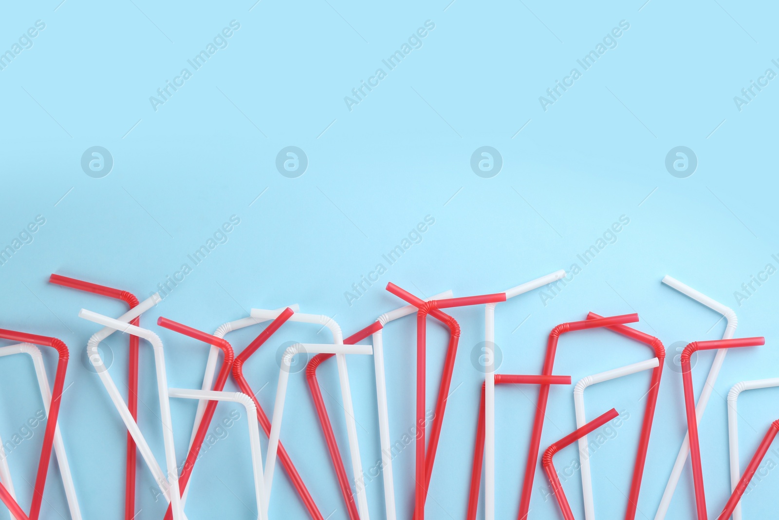 Photo of Colorful plastic drinking straws on light blue background, flat lay. Space for text