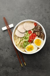 Photo of Delicious ramen with meat in bowl and chopsticks on grey textured table, top view. Noodle soup