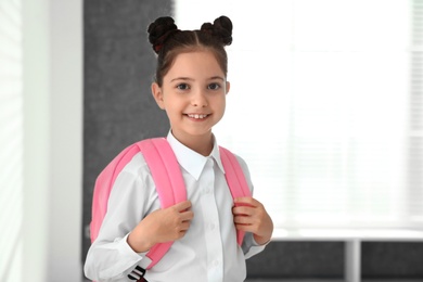 Happy girl in school uniform with backpack indoors