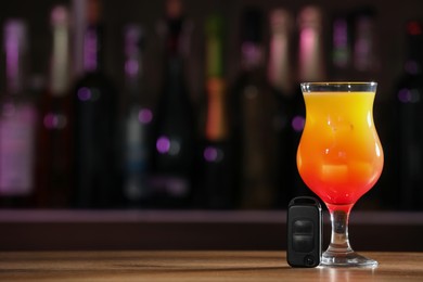 Photo of Car key and glass of alcoholic drink on table against blurred background, space for text. Drunk driving concept