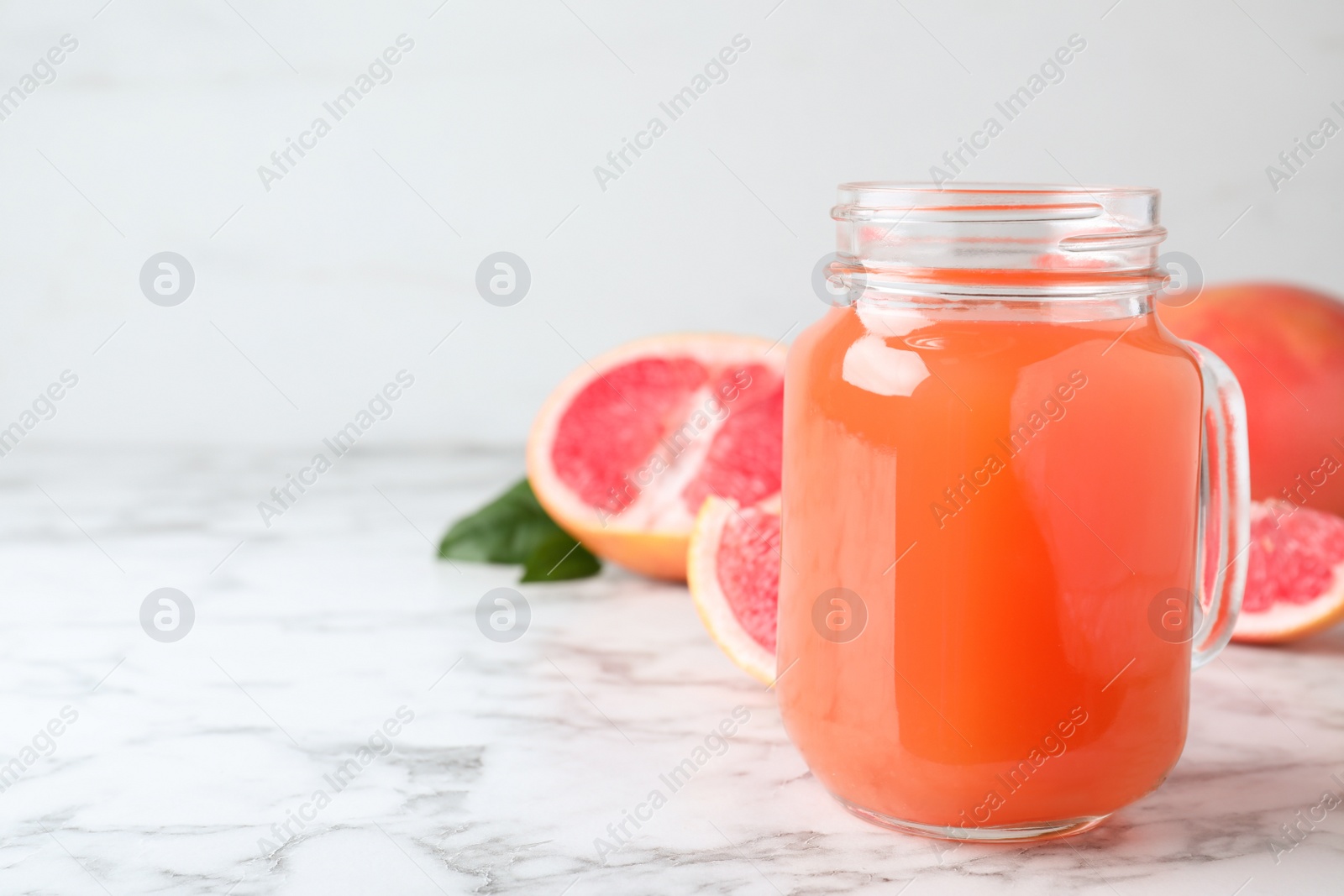 Photo of Tasty freshly made grapefruit juice on white marble table. Space for text