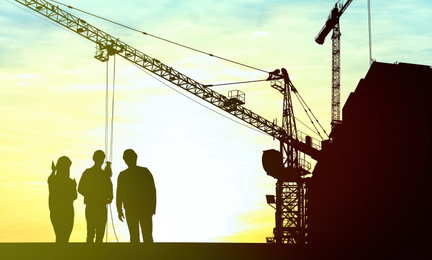 Silhouettes of engineers near construction site at sunrise