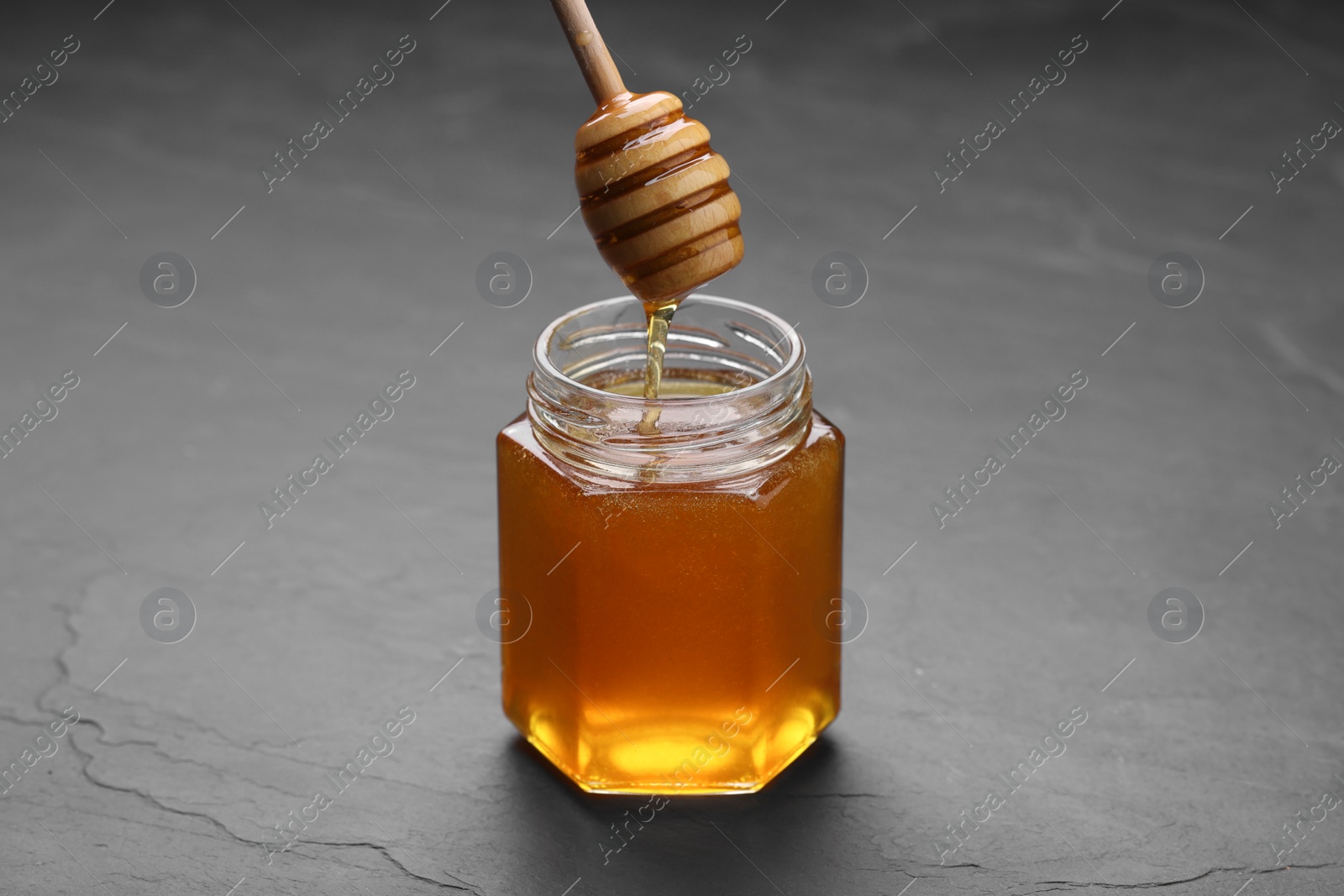 Photo of Pouring sweet honey from dipper into jar at grey textured table