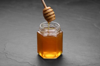 Photo of Pouring sweet honey from dipper into jar at grey textured table