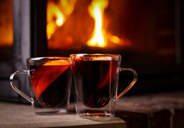 Tasty mulled wine in glass cups near fireplace indoors