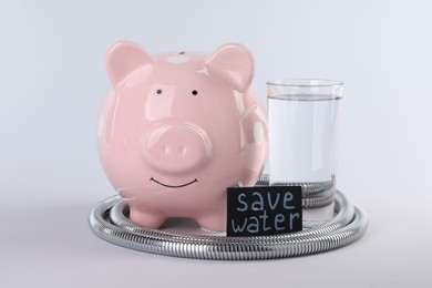 Photo of Water scarcity concept. Card with phrase Save Water, piggy bank, shower hose and glass of drink isolated on white