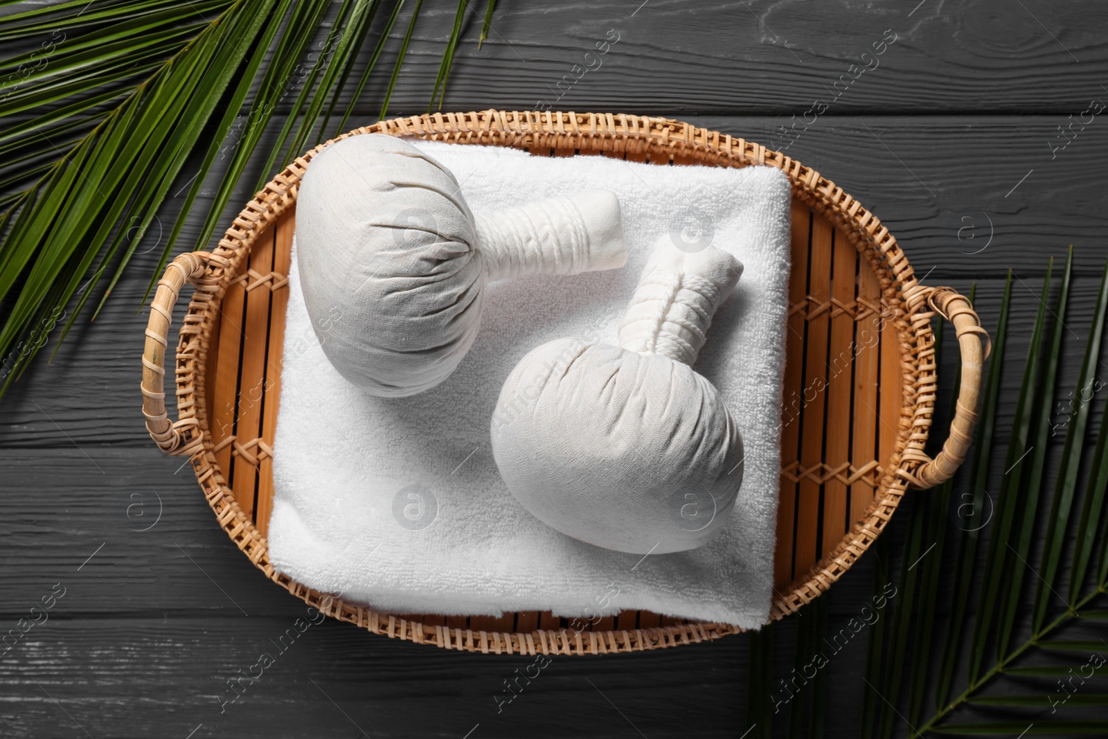 Photo of Herbal massage bags, towel and palm leaves on grey wooden table, top view and space for text. Spa procedure
