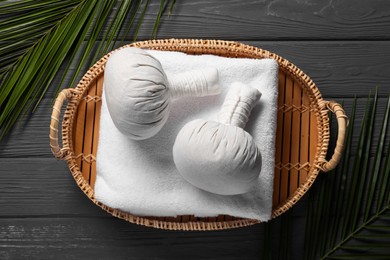Herbal massage bags, towel and palm leaves on grey wooden table, top view and space for text. Spa procedure