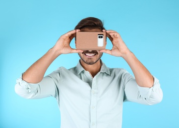 Photo of Young man using cardboard virtual reality headset on color background