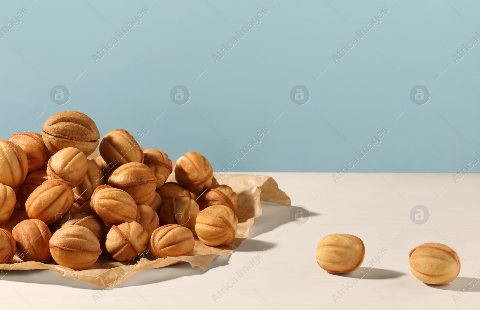 Photo of Freshly baked walnut shaped cookies on white wooden table against light blue wall, space for text. Homemade pastry filled with caramelized condensed milk