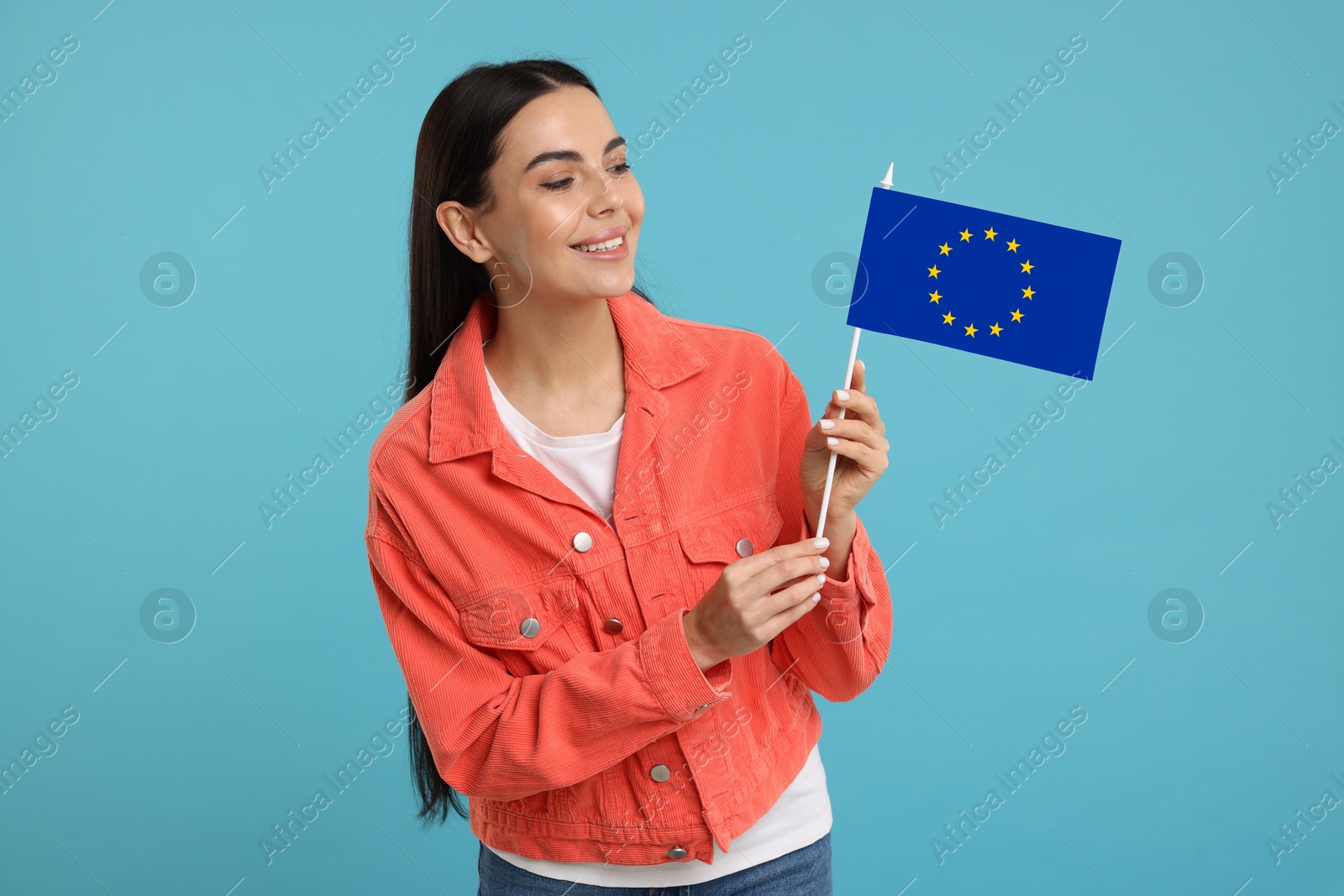 Image of Happy young woman with flag of European Union on light blue background