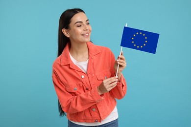 Happy young woman with flag of European Union on light blue background