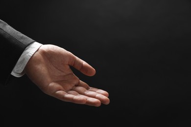 Man holding something in hand on black background, closeup. Space for text