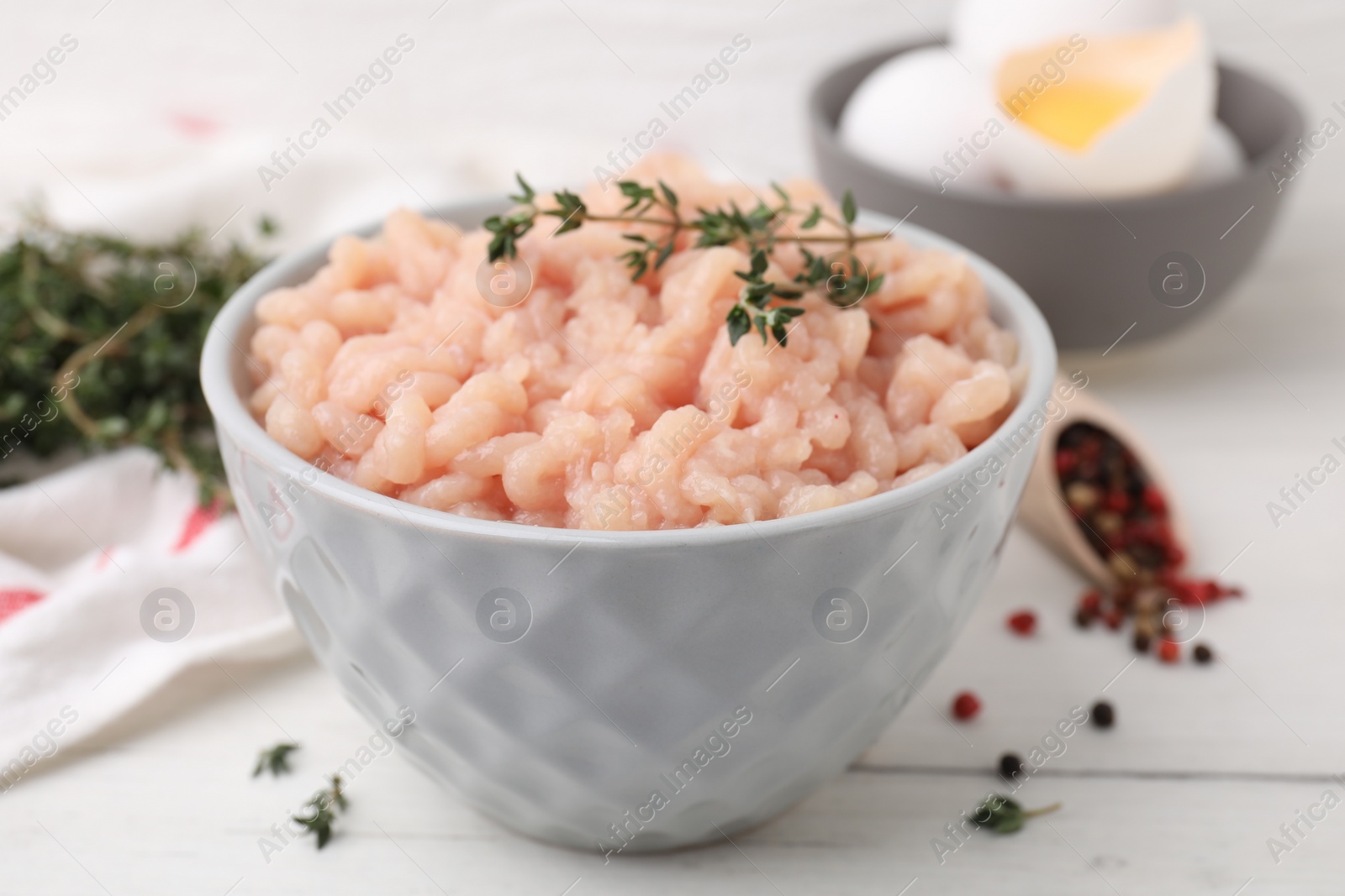 Photo of Fresh raw minced meat and thyme in bowl on white wooden table, closeup
