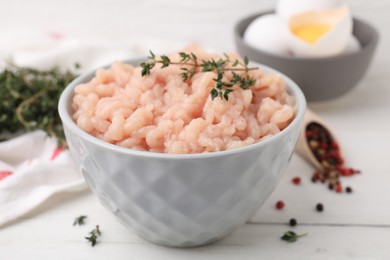 Fresh raw minced meat and thyme in bowl on white wooden table, closeup