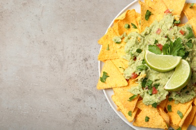 Photo of Plate of delicious mexican nachos chips with guacamole sauce and lime on grey table, top view. Space for text