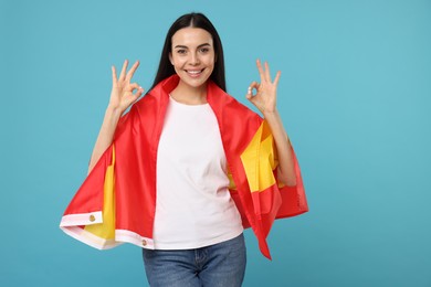 Photo of Happy young woman with flag of Spain showing OK gesture on light blue background