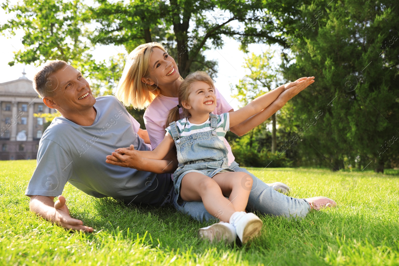 Photo of Happy parents with their child having fun on green grass. Spending time in nature