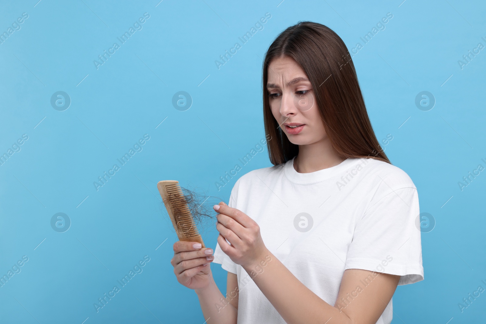 Photo of Upset woman untangling her lost hair from comb on light blue background, space for text. Alopecia problem