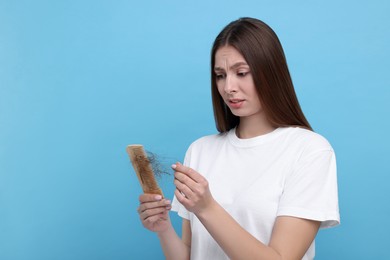 Photo of Upset woman untangling her lost hair from comb on light blue background, space for text. Alopecia problem