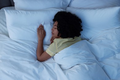 Photo of Young woman sleeping in soft bed at night, top view