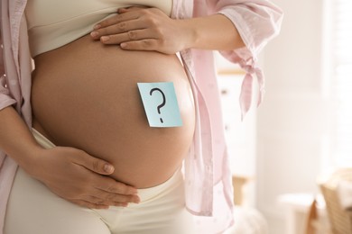 Pregnant woman with sticky note on belly indoors, closeup. Choosing baby name