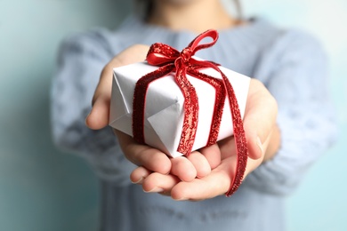 Photo of Woman holding beautiful Christmas gift on light blue background, closeup