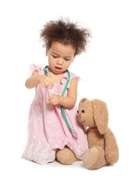 Photo of Cute African American child imagining herself as doctor while playing with stethoscope and toy bunny on white background