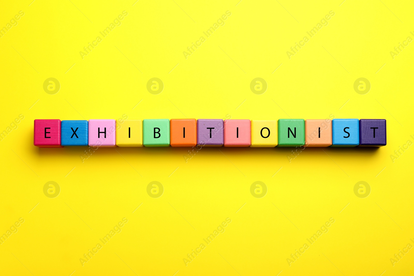 Photo of Word EXHIBITIONIST made with colorful cubes on yellow background, flat lay
