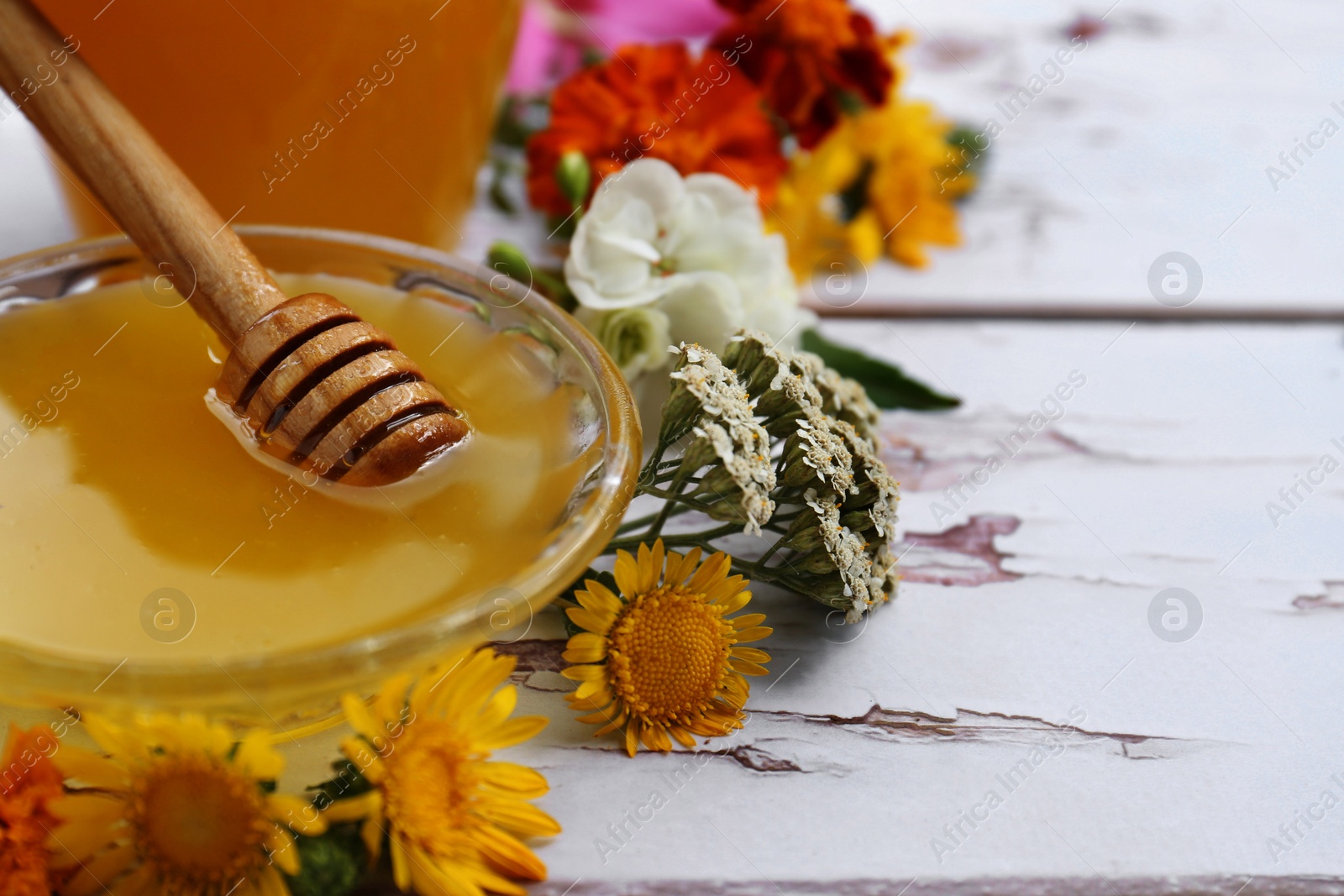 Photo of Honey with dipper in bowl and different flowers on white wooden table, closeup. Space for text