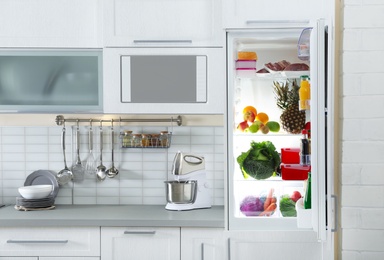 Photo of Open refrigerator full of products in stylish kitchen interior