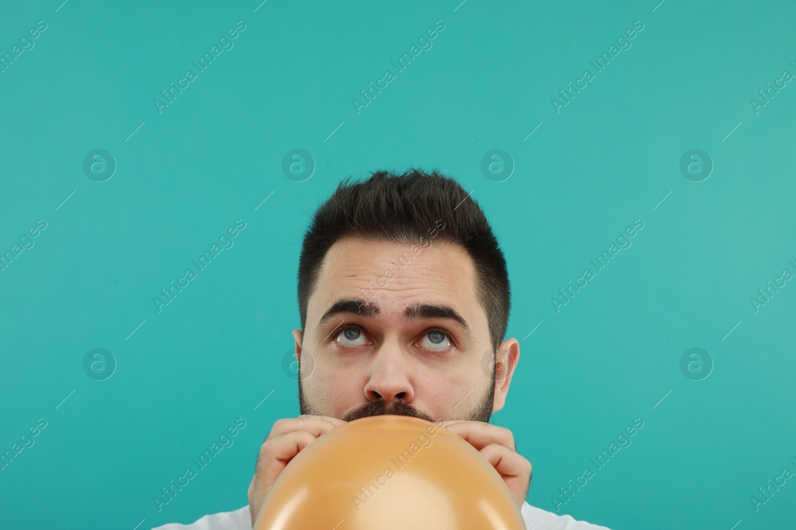 Photo of Man inflating bright balloon on turquoise background