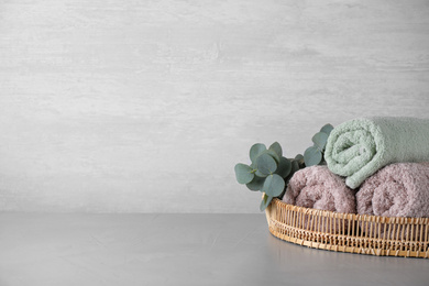 Photo of Wicker tray with rolled bath towels and eucalyptus branch on grey table. Space for text