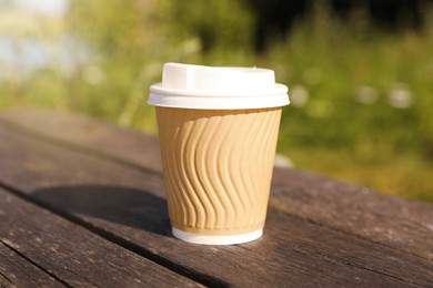 Paper cup on wooden bench outdoors, closeup. Coffee to go