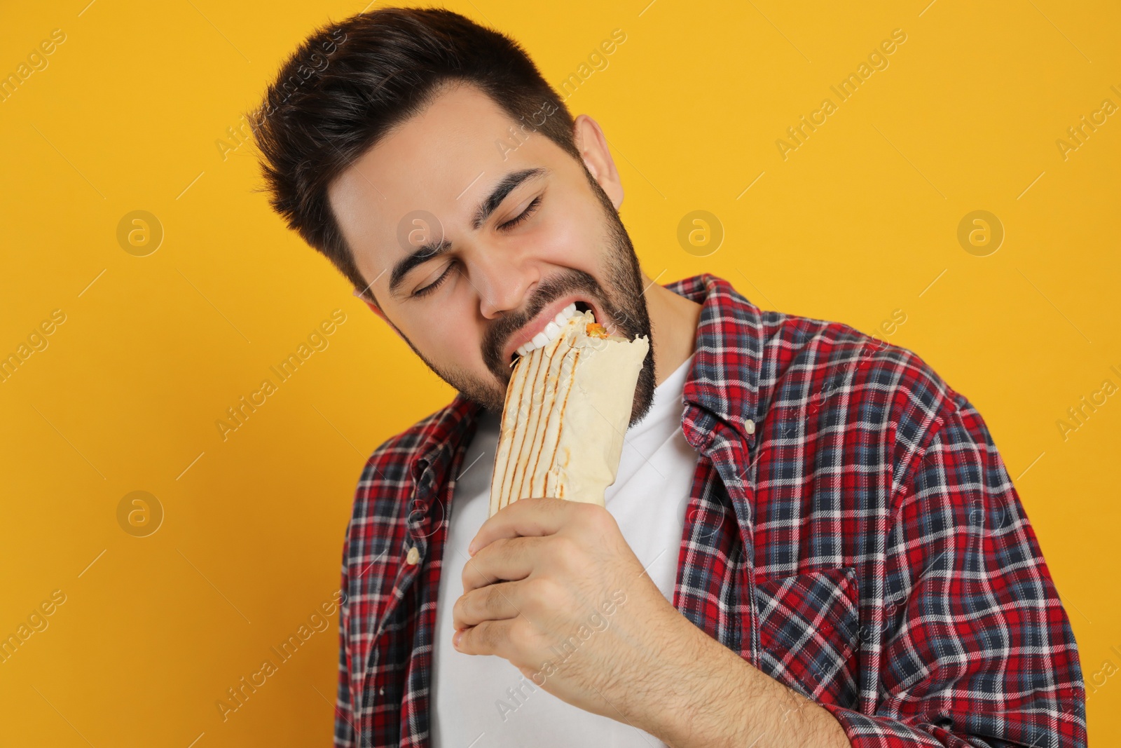 Photo of Young man eating tasty shawarma on yellow background