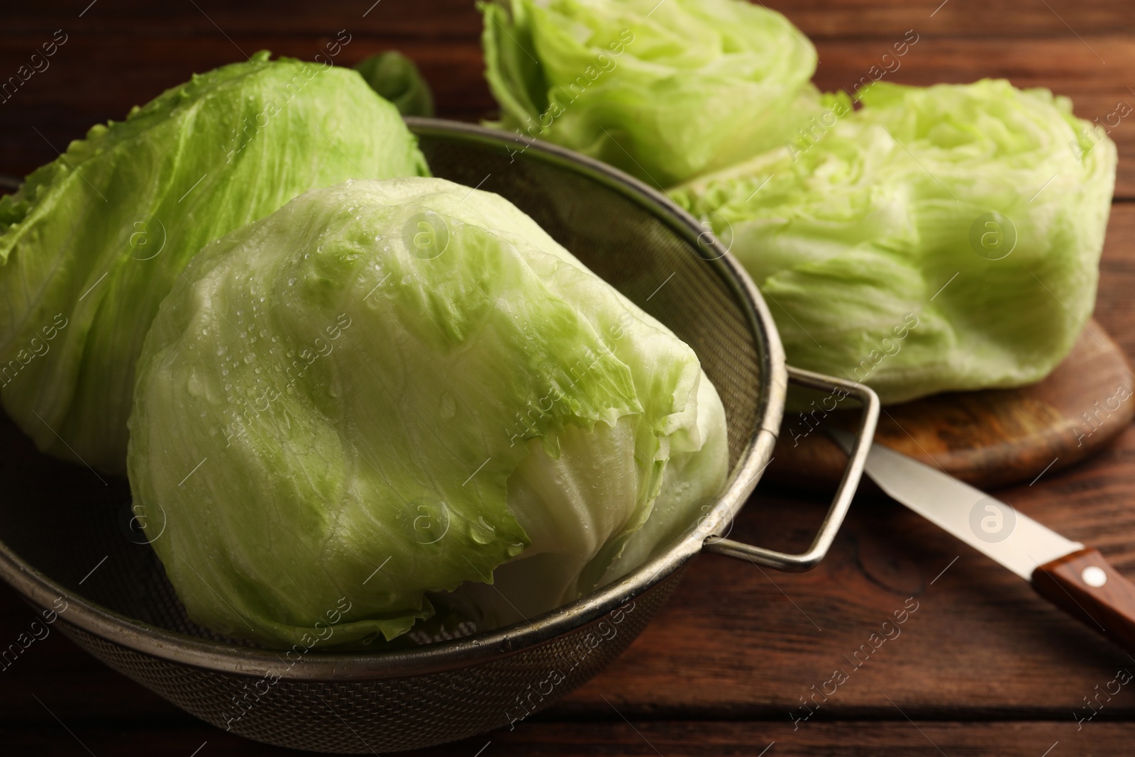 Photo of Colander with fresh green wet iceberg lettuce heads on wooden table, closeup