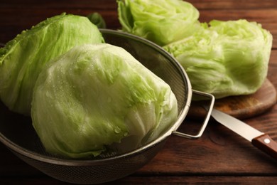 Photo of Colander with fresh green wet iceberg lettuce heads on wooden table, closeup