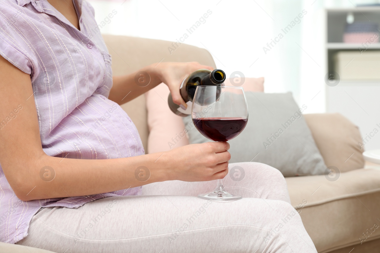 Photo of Future mother pouring wine from bottle into glass at home, closeup. Alcohol abuse during pregnancy