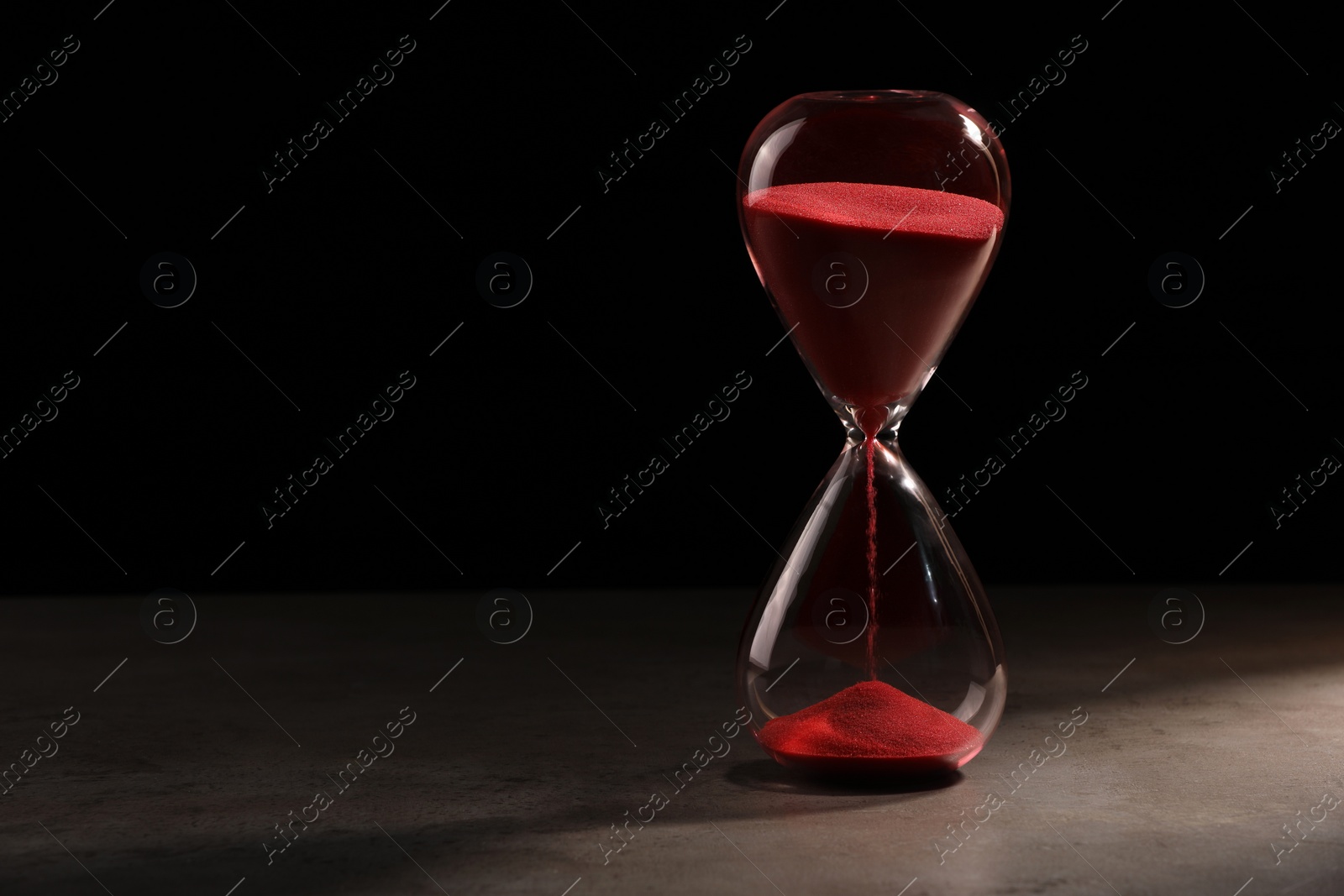 Photo of Hourglass with red flowing sand on grey table. Space for text