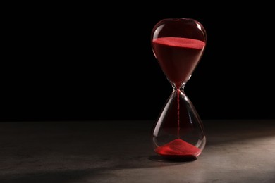 Photo of Hourglass with red flowing sand on grey table. Space for text