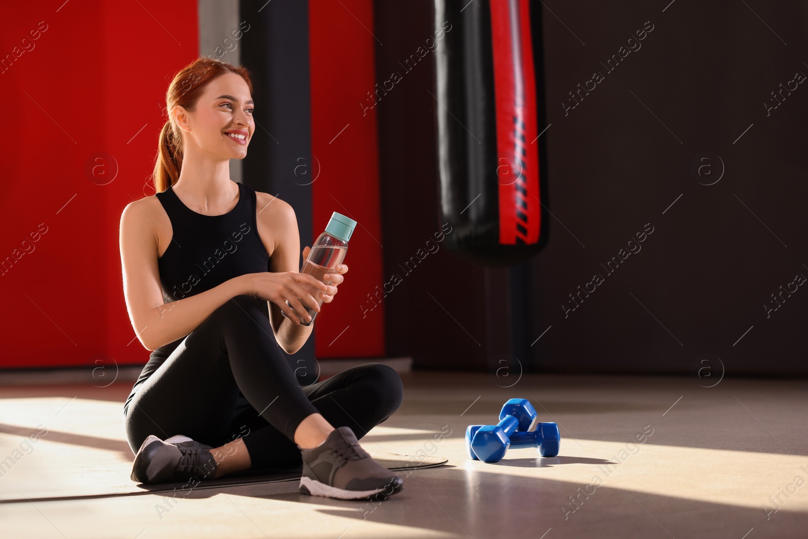 Photo of Athletic young woman with bottle of water on mat in gym, space for text