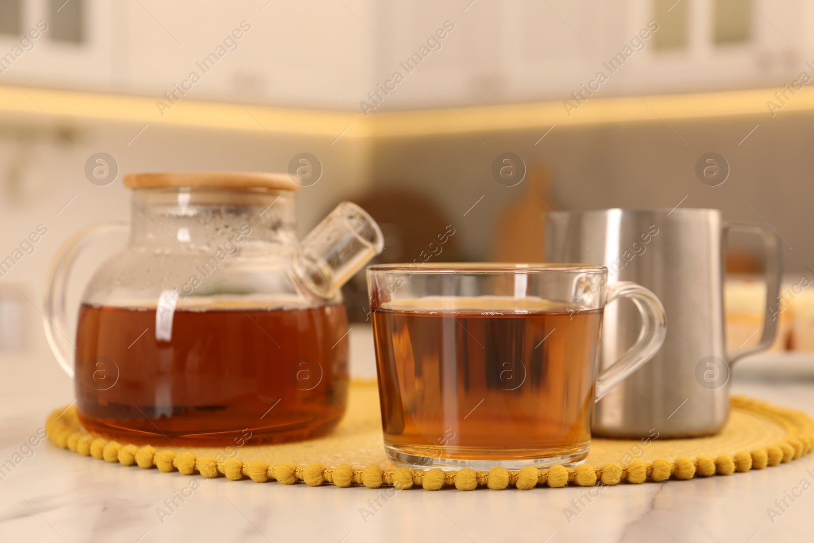 Photo of Aromatic tea in glass teapot, cup and pitcher on light marble table