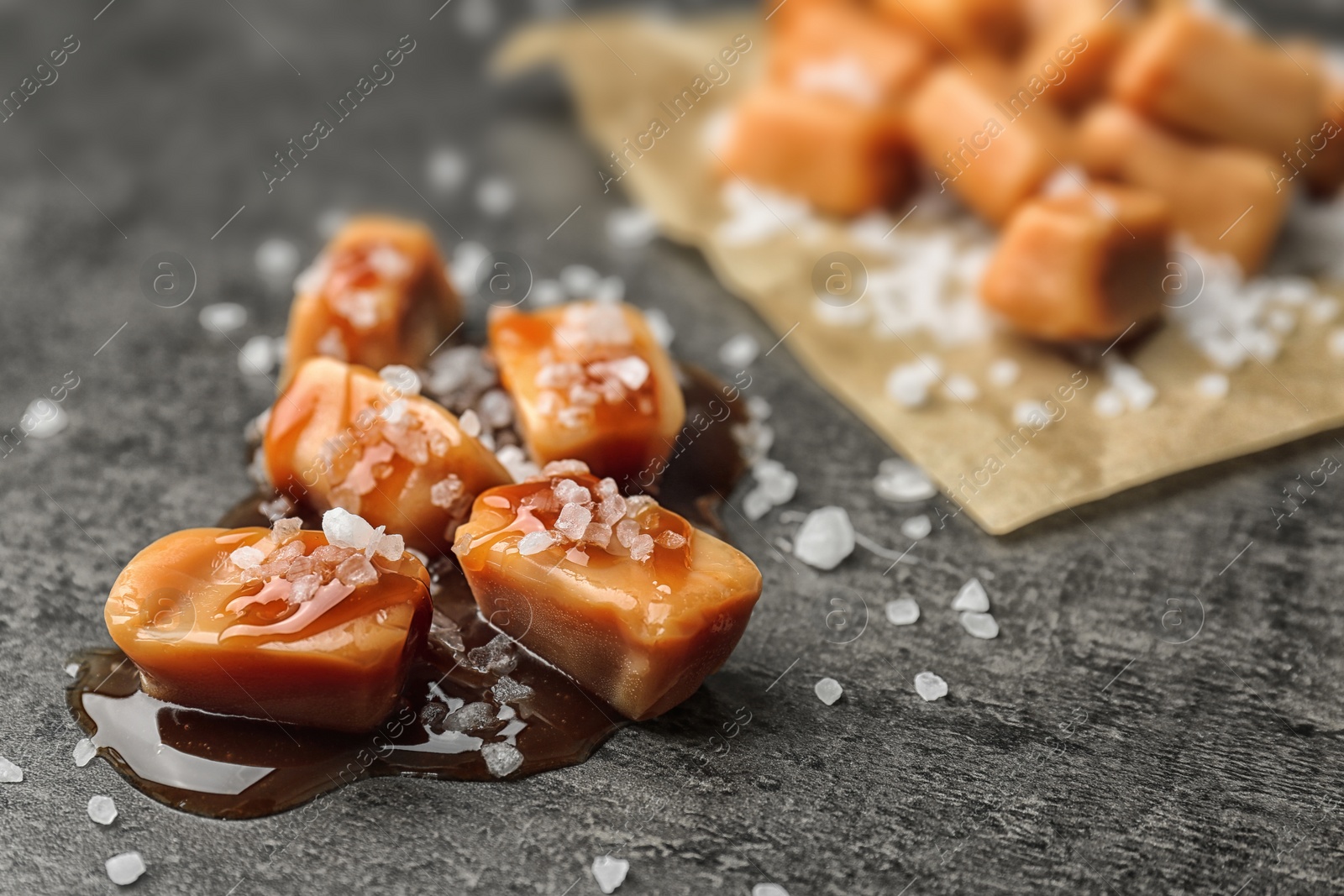 Photo of Delicious candies with caramel sauce and salt on gray background