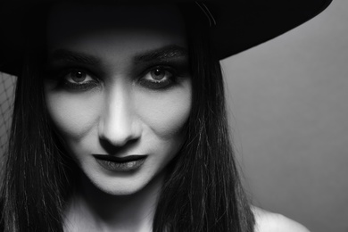Photo of Mysterious witch wearing hat on dark background, closeup. Black and white effect