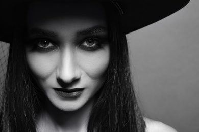 Mysterious witch wearing hat on dark background, closeup. Black and white effect