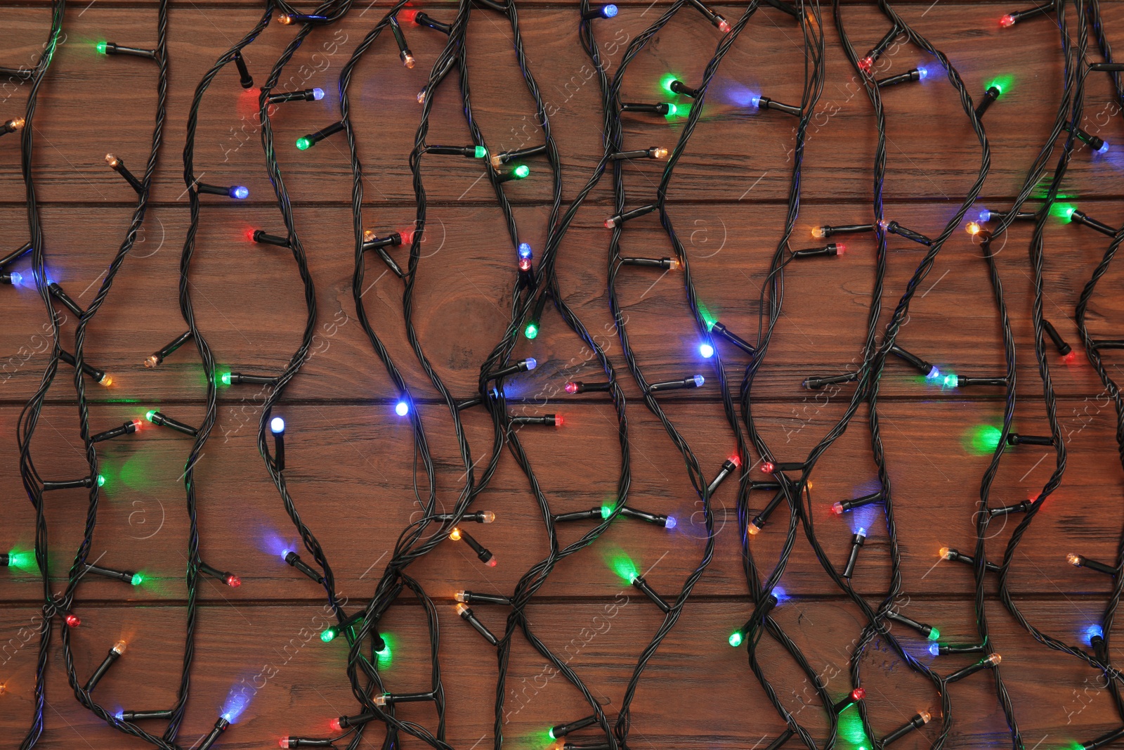 Photo of Glowing Christmas lights on wooden background, top view