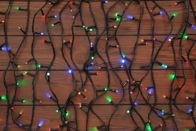 Glowing Christmas lights on wooden background, top view