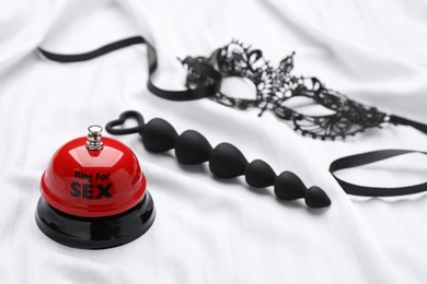 Anal beads, bell with text Ring For Sex and black lace mask on white fabric