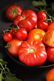 Photo of Many different ripe tomatoes with leaves on black table, closeup